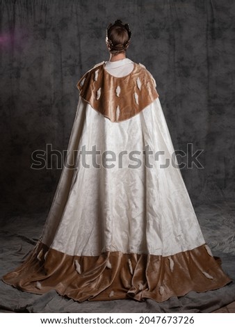 The young king. A noble young man in a fantasy historical costume, in a fur robe and with a crown on his head. The prince becomes the king, Full-length fur mantle back view