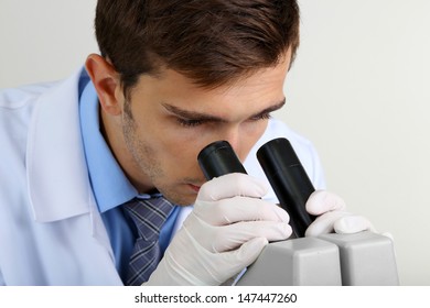 Young laboratory scientist looking at microscope in lab