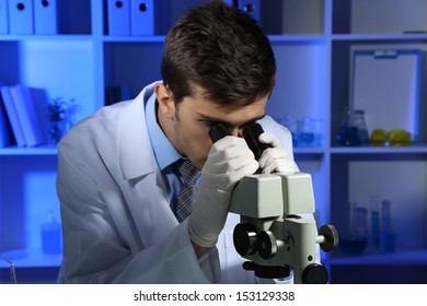 Young Laboratory Scientist Looking At Microscope In Lab 