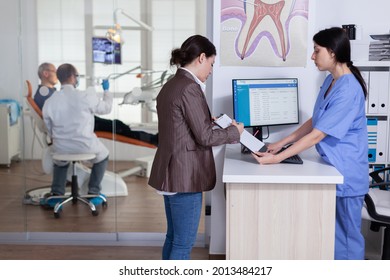 Young lady asking informations filling in stomatological form while patients talking sitting on chair in waiting area. People speaking in crowded professional orthodontist reception office. - Powered by Shutterstock