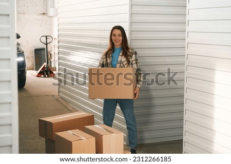 Young lady with big cardboard boxes into warehouse with self storage unit