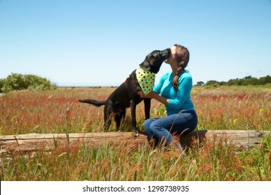 Young Lady With Black Dog Kissing Face On Log In Field