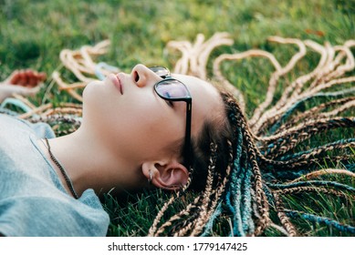 Young lady with box braids is lying on grass with eyes closed
