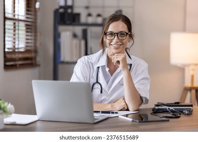 Young lady doctor in white medical uniform using laptop talking video conference call with senior doctor at desk,Doctor sitting at desk and writing a prescription for her patient - Powered by Shutterstock