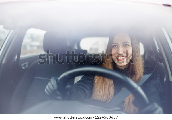 Young lady driving a car in winter.\
Smiling woman steering car view through\
windshield