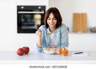 Young lady eating healthy oatmeal, sitting at modern kitchen interior, enjoying granola with milk for breakfast, free space. Healthy lifestyle, diet, nutrition concept - Powered by Shutterstock