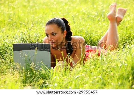 Young lady enjoys spring with her laptop in the green fresh grass