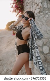 Young Lady, Girl Wearing Sexy Black Bikini, Swimsuit With Hight Waist, Cardigan, Cape With Ornaments. Beautiful Beach, Flowers, Rock On Background.