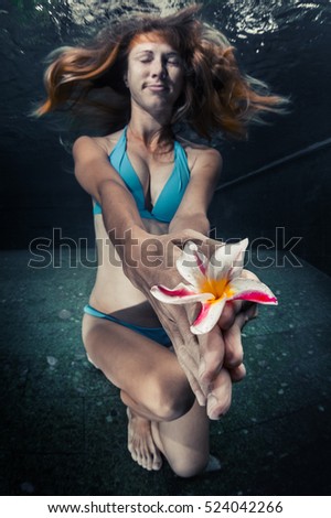 Young lady holding the flower underwater in the pool