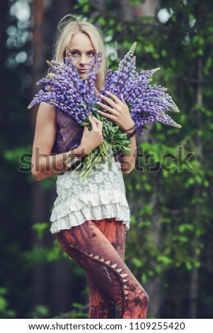 young lady holding wild flowers bouquet, posing for portraits in the forest on a summer evening