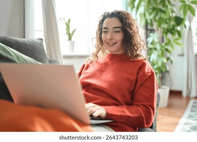 Young lady looking at computer ordering sale products on website, watching videos or elearning. Relaxed happy woman sitting on couch using laptop at home surfing, doing online ecommerce shopping,
