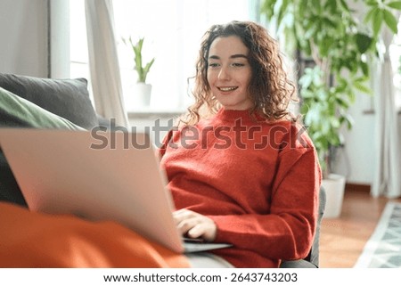 Young lady looking at computer ordering sale products on website, watching videos or elearning. Relaxed happy woman sitting on couch using laptop at home surfing, doing online ecommerce shopping,