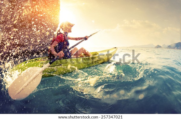 Young lady paddling hard the kayak with lots\
of splashes near the cliff at sunny\
day