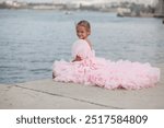 A young lady in a pink princess dress poses on the street, a 7-year-old child model walks along the street of an ancient city. Concept of a postcard 