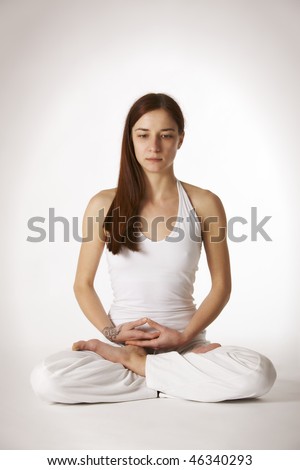 Young lady practicing yoga in lotus posture (Padmasana) looking downwards in white clothes on white background, high-key image.