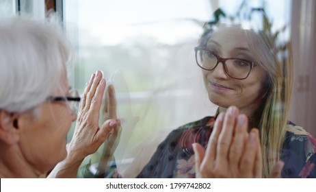 Young Lady In Quarantine Speaking With Her Grandmother Through The Glass Window. Protecting Vulnerable From Covid Infection. 