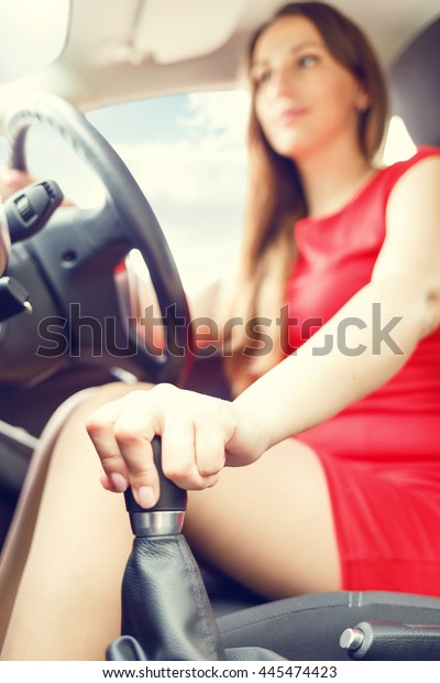 Young lady in red dress driving\
car. Driving school background. Pretty woman switch stick\
shift