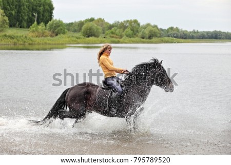 Young lady rider galloping through water 