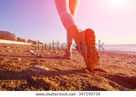 Young lady running on the beach at sunrise. shoes closeup