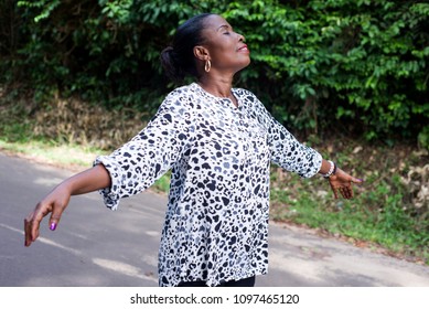 young lady standing in black white shirt with outstretched arms breathing fresh air smiling with eyes closed.