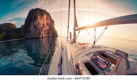 Young lady standing on the bow of yacht and looking to the rocky island at sunrise