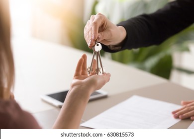 Young lady taking keys from female real estate agent during meeting after signing rental lease contract or sale purchase agreement. Independent woman purchasing new home, close up view
