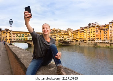 Young Lady Taking Selfie In Front Of Ponte Vecchio Bridge In Florence Tuscany Italy, During Her Summer Vacations In Europe.