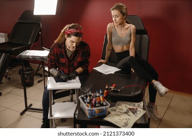 Young lady in top sitting on chair in tattoo salon and waiting for tattoo artist preparing drawing