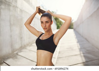 Young lady tying her hair just before her everyday everning workout on a sunny summer day in concrete jungle. Urban sport concept. - Powered by Shutterstock