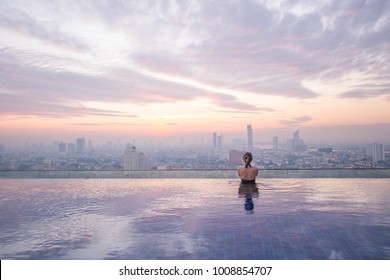 Young Lady Watching The Sunrise At The Infinity Pool With City View. Bangkok, Thailand.