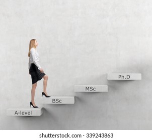 Young Lady Woman Is Going Up To The Stairs. Steps Symbolise Level Of Education. A-levle, Bachelor, Masters And Doctor Of Philosophy. Concrete Background. Education.