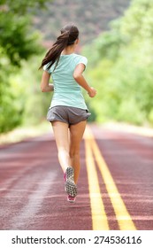 Young Lady Working Out Running Away On Rural Road. Woman Runner Athlete Training Jogging During Workout Outside. Full Body Length Rear View Showing Back. Girl In Shorts And Running Shoes.