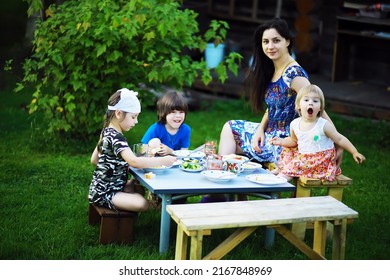 A Young Large Family At A Picnic On A Summer Morning. A Beautiful Mother With Children Is Having Breakfast In The Park.