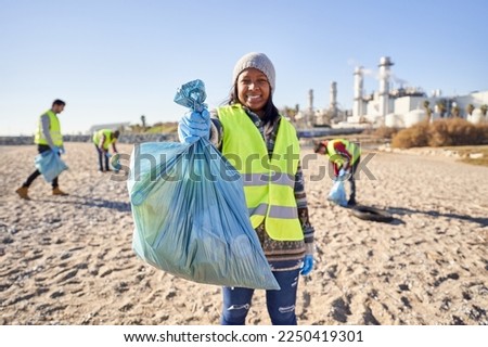 Young latin activist looking at camera holding a garbage bag trash. Group of cleanup volunteers cleaning up waste in nature on sunny day. Concept of environmental protection.