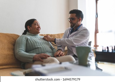 Young Latin American Doctor Checking Patient At Home. Doctor Checking Heartbeat Of Patient . Doctor Doing Home Service. Healthcare Concept.