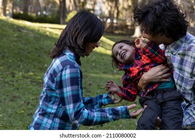 Young Latin American Family Spend The Afternoon In The Park While Happily Playing With Their 3 Year Old Child. Family Concept.