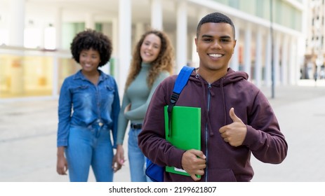 Young Latin American Male Student With Backpack And Group Of International Students Outdoor In Summer In City