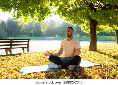 A young Latin American man is doing yoga in the morning in the park. Sitting on a mat in the lotus position with closed eyes and meditating. - Powered by Shutterstock