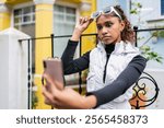 Young latin american woman adjusting her sunglasses with a surprised expression while taking a selfie with her smartphone