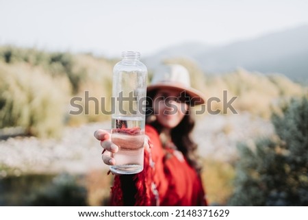 Young latin american woman using traditional clothes, holding a glass bottle with water.
