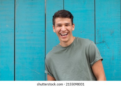 Young Latin With An Authentic Laugh, In The Background A Blue Door Typical Of Latin Homes. Latin Representation In A Portrait.