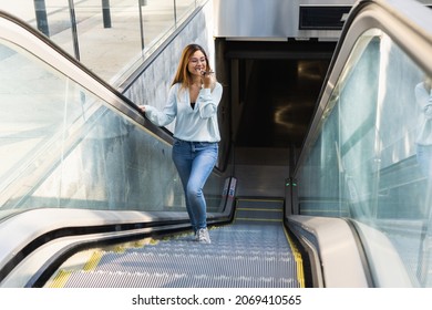 Young latin businesswoman with glasses using smartphone, going up on metro, subway, airport escalator. Business concept