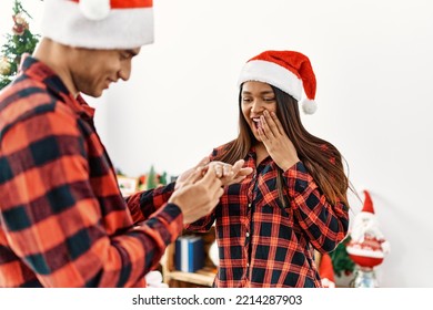 Young Latin Couple Celebrating Christmas Holding Engagement Ring For Wedding Proposal At Home.