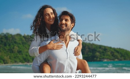 Young Latin couple creates a lasting memory of joy as the woman playfully hops on the man's back for a ride along the beach, their smiles lighting up the scene with pure happiness.