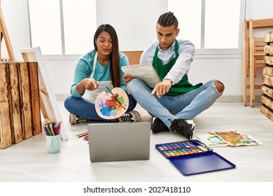 Young Latin Couple Having Online Paint Class At Art Studio Pointing With Finger To The Camera And To You, Confident Gesture Looking Serious 