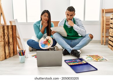 Young Latin Couple Having Online Paint Class At Art Studio Serious Face Thinking About Question With Hand On Chin, Thoughtful About Confusing Idea 