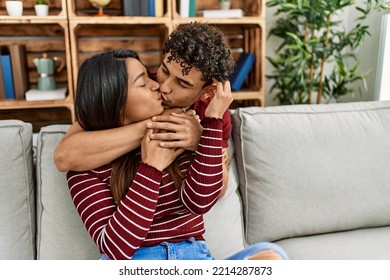 Young Latin Couple Kissing And Hugging Sitting On The Sofa At Home.