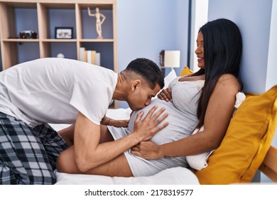 Young Latin Couple Kissing Tummy Lying On Bed At Bedroom