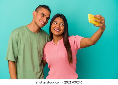 Young Latin Couple With A Mobile Phone Isolated On Blue Background