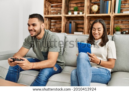 Young latin couple playing video game and using touchpad at home.